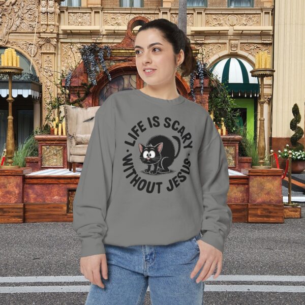 Model on a Halloween set wearing a gray Life is Scary Without Jesus Halloween Sweatshirt, design showing a cute frightened black cat.