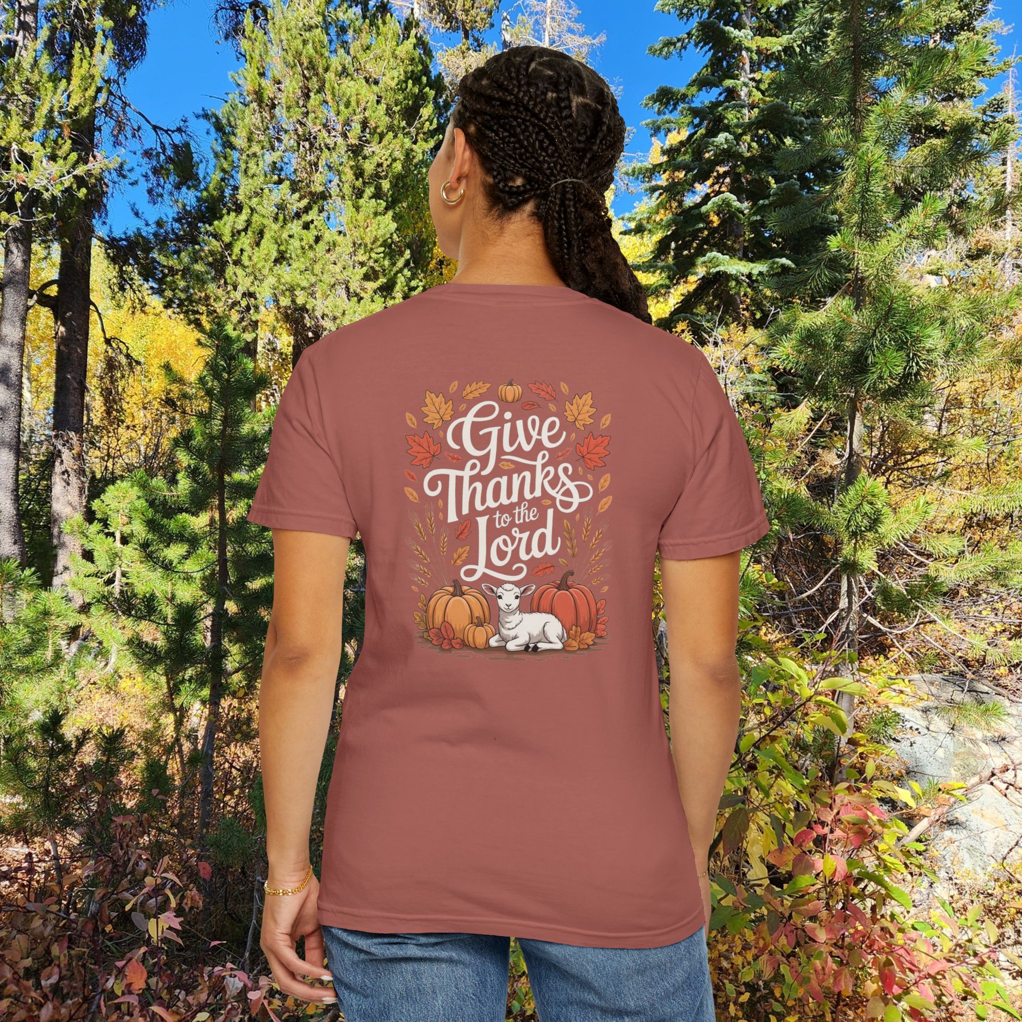 Model in a woods setting wearing a red Give Thanks to the Lord t-shirt with Thanksgiving design showing a lamb, pumpkins, and fall leaves.