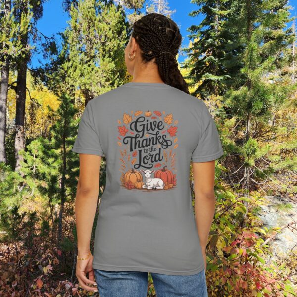 Model in a woods setting wearing a Gray Give Thanks to the Lord t-shirt with Thanksgiving design showing a lamb, pumpkins, and fall leaves.