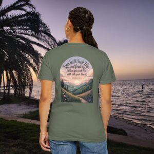 Green Christian t-shirt with Jeremiah 29:13 scripture, mountain valley, and sunset graphic, worn by a person in a serene beach setting.