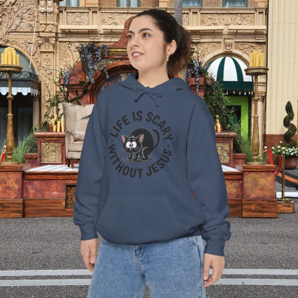 Model on a Halloween set wearing a blue Life is Scary Without Jesus Halloween Hoodie, design showing a cute frightened black cat.