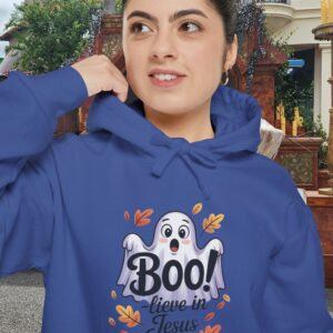 Model on a Halloween set wearing a Blue Boo! -lieve in Jesus Halloween Hoodie, design showing a cute ghost with fall leaves.