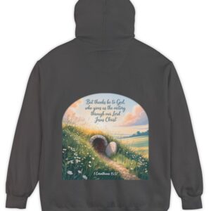 Dark grey Comfort Colors hoodie sweatshirt with a field and an open tomb with the rock rolled away. Printed on it is 1 Corinthians 15:57 But thanks be to God, who gives us the victory through our Lord Jesus Christ.