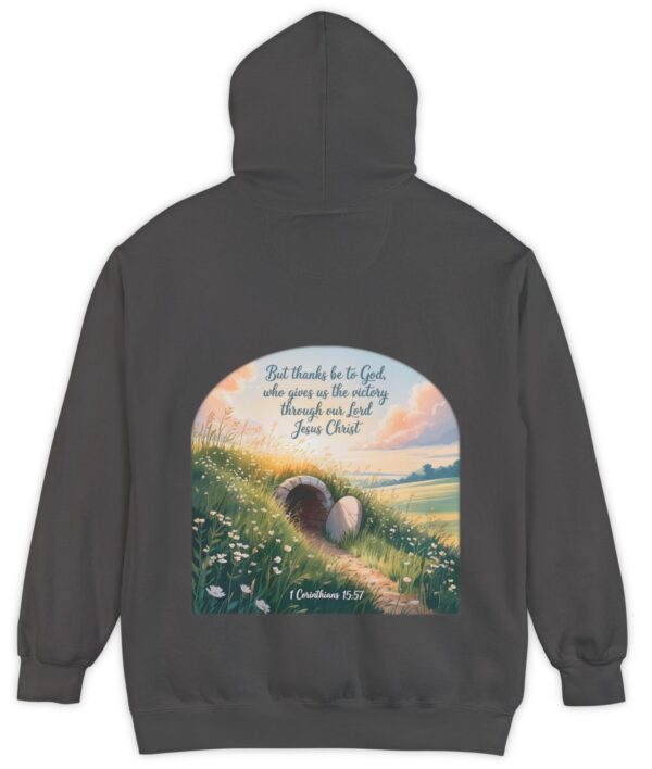 Dark grey Comfort Colors hoodie sweatshirt with a field and an open tomb with the rock rolled away. Printed on it is 1 Corinthians 15:57 But thanks be to God, who gives us the victory through our Lord Jesus Christ.