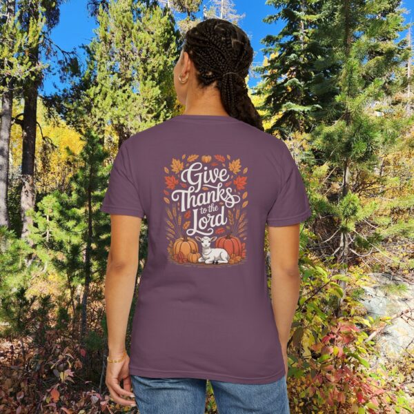Model in a woods setting wearing a Purple Give Thanks to the Lord t-shirt with Thanksgiving design showing a lamb, pumpkins, and fall leaves.