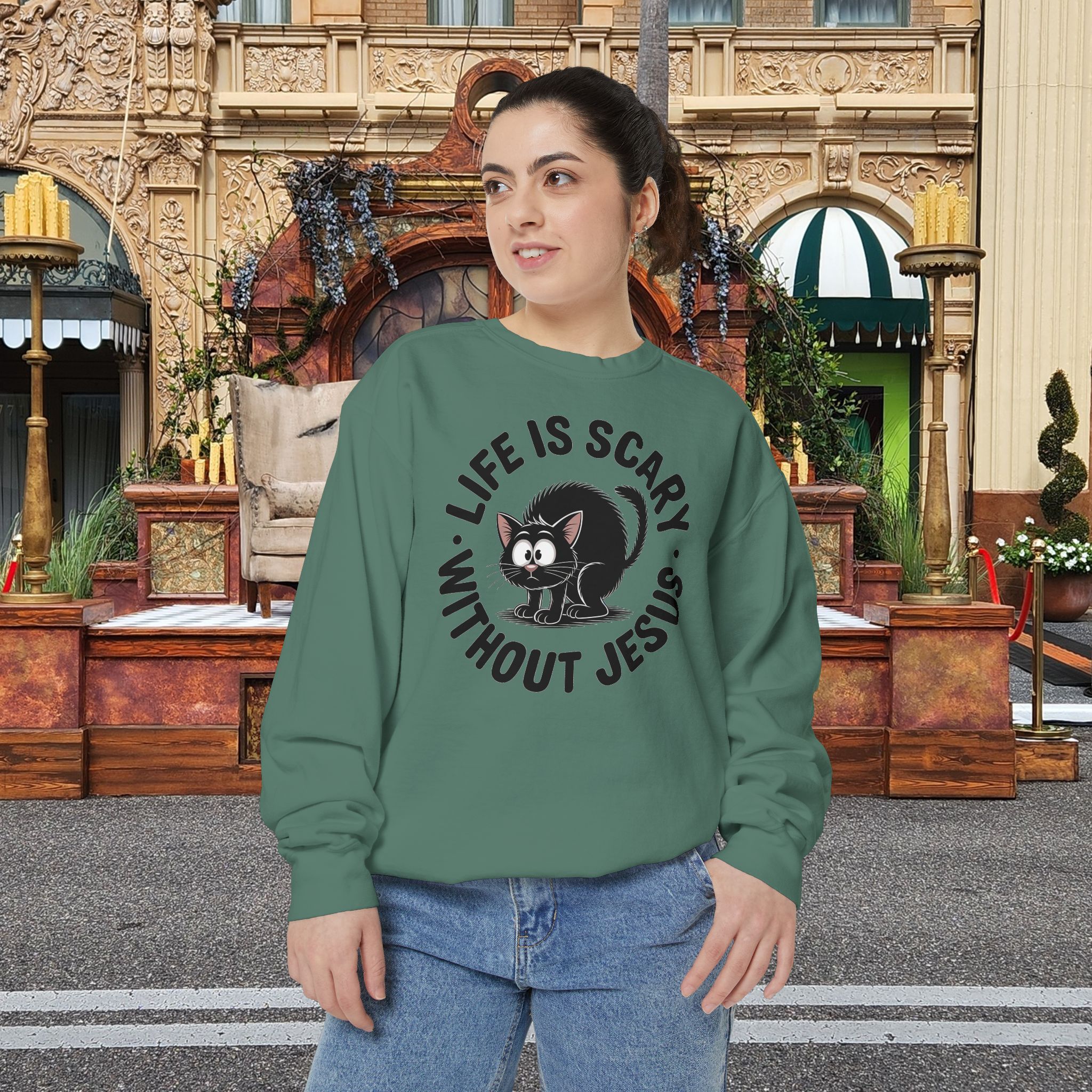 Model on a Halloween set wearing a green Life is Scary Without Jesus Halloween Sweatshirt, design showing a cute frightened black cat.