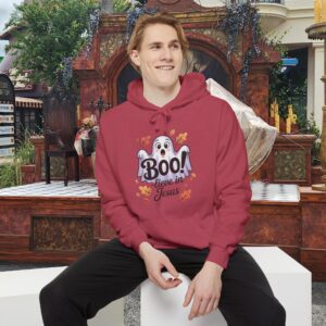 Model on a Halloween set wearing a red Boo! -lieve in Jesus Halloween Hoodie, design showing a cute ghost with fall leaves.