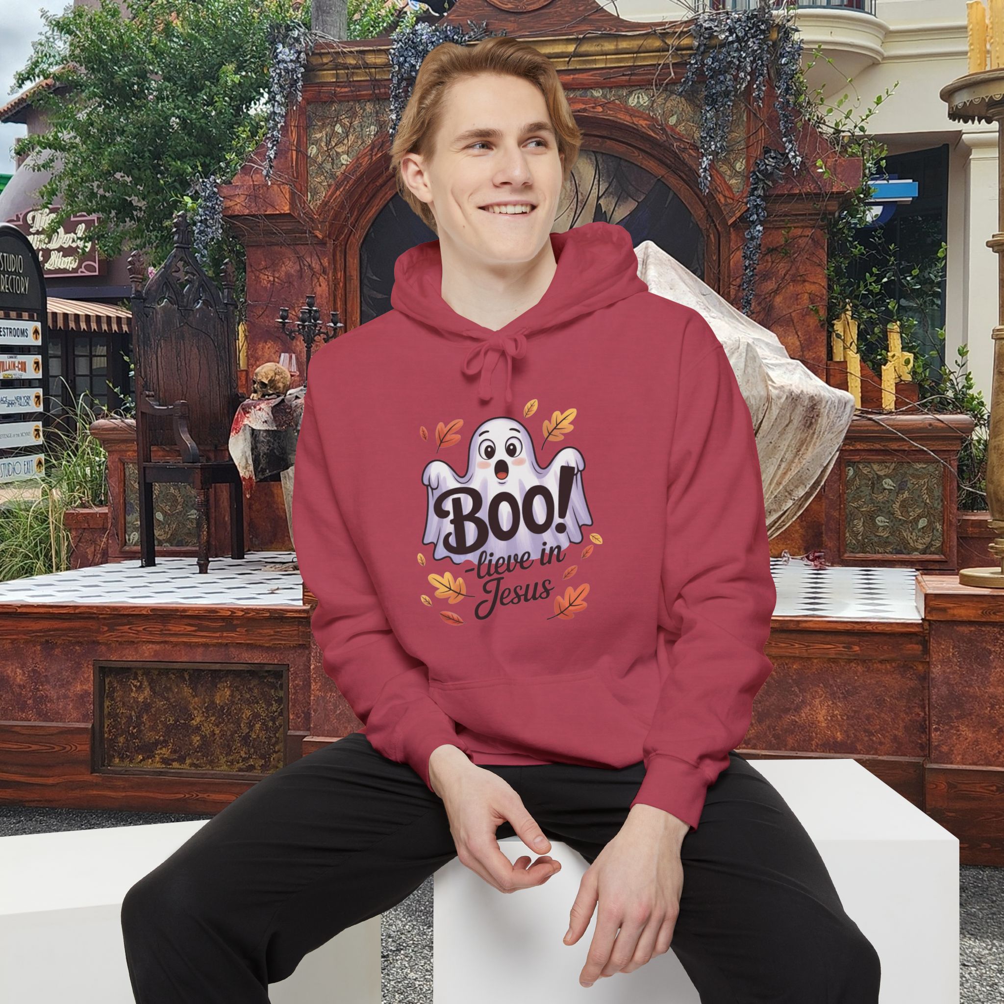 Model on a Halloween set wearing a red Boo! -lieve in Jesus Halloween Hoodie, design showing a cute ghost with fall leaves.