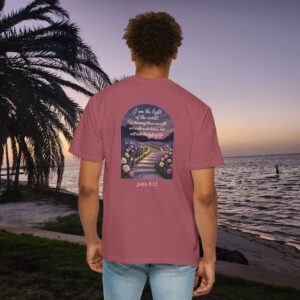 Pink Christian t-shirt with John 8:12 scripture, lit stairway path with flowers and sunset design, worn by a person standing on a sunset beach.