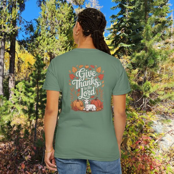 Model in a woods setting wearing a Green Give Thanks to the Lord t-shirt with Thanksgiving design showing a lamb, pumpkins, and fall leaves.
