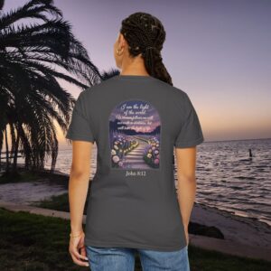 Gray Christian t-shirt with John 8:12 scripture, lit stairway path with flowers and sunset design, worn by a person standing on a sunset beach.