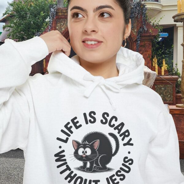 Model on a Halloween set wearing a white Life is Scary Without Jesus Halloween Hoodie, design showing a cute frightened black cat.