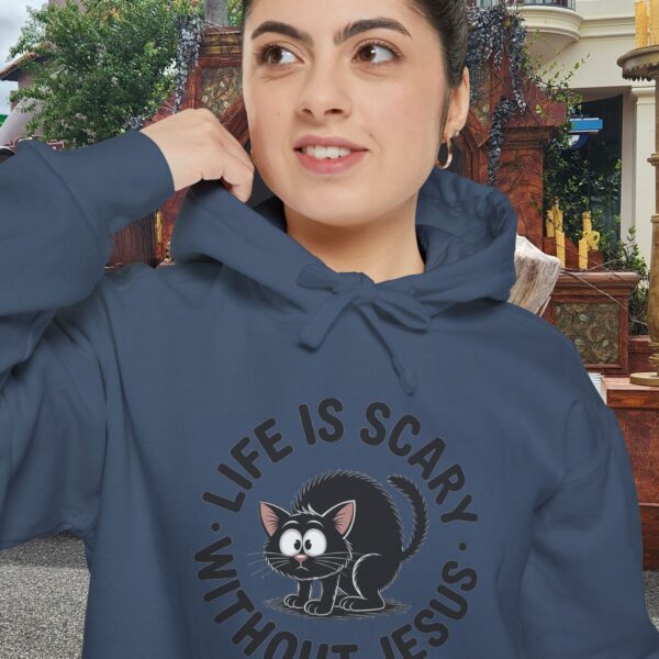 Model on a Halloween set wearing a blue Life is Scary Without Jesus Halloween Hoodie, design showing a cute frightened black cat.