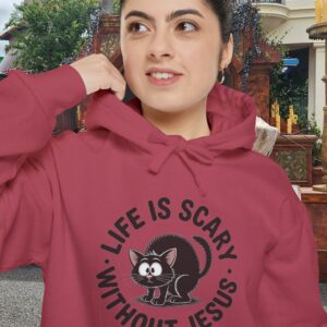 Model on a Halloween set wearing a red Life is Scary Without Jesus Halloween Hoodie, design showing a cute frightened black cat.