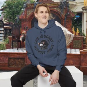 Model on a Halloween set wearing a blue Life is Scary Without Jesus Halloween Hoodie, design showing a cute frightened black cat.