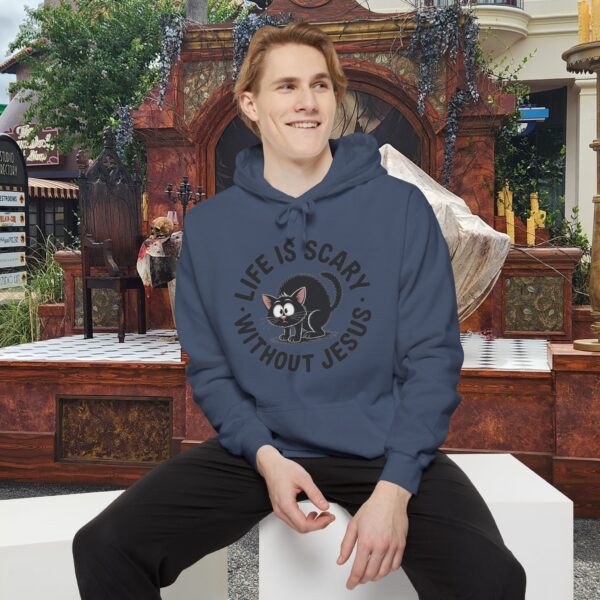 Model on a Halloween set wearing a blue Life is Scary Without Jesus Halloween Hoodie, design showing a cute frightened black cat.