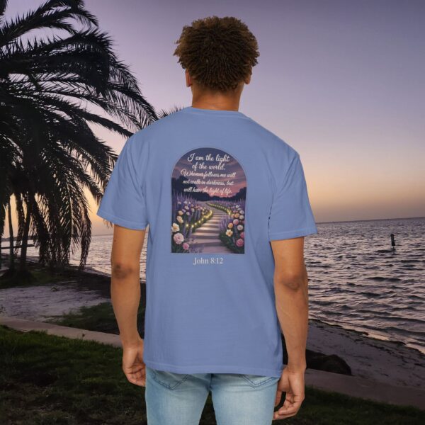 Blue Christian t-shirt with John 8:12 scripture, lit stairway path with flowers and sunset design, worn by a person standing on a sunset beach.