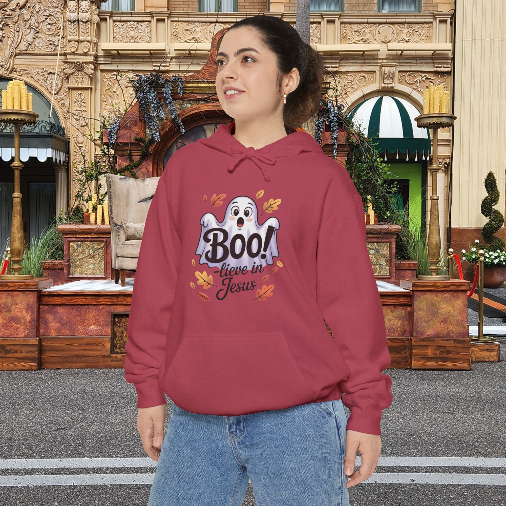 Model on a Halloween set wearing a red Boo! -lieve in Jesus Halloween Hoodie, design showing a cute ghost with fall leaves.
