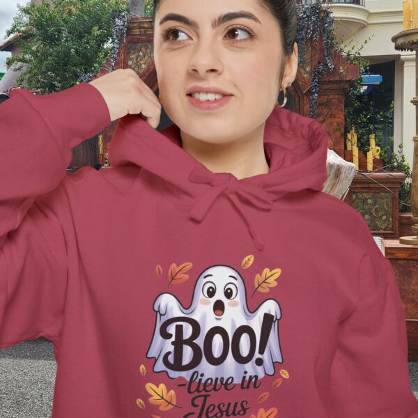 Model on a Halloween set wearing a red Boo! -lieve in Jesus Halloween Hoodie, design showing a cute ghost with fall leaves.
