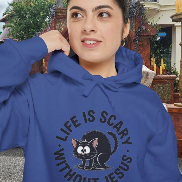 Model on a Halloween set wearing a blue Life is Scary Without Jesus Halloween Hoodie, design showing a cute frightened black cat.