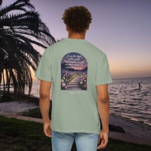 Green Christian t-shirt with John 8:12 scripture, lit stairway path with flowers and sunset design, worn by a person standing on a sunset beach.