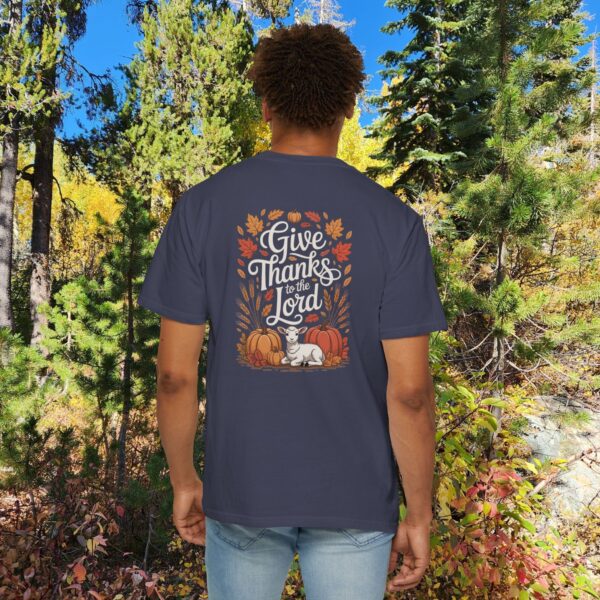 Model in a woods setting wearing a Gray Give Thanks to the Lord t-shirt with Thanksgiving design showing a lamb, pumpkins, and fall leaves.