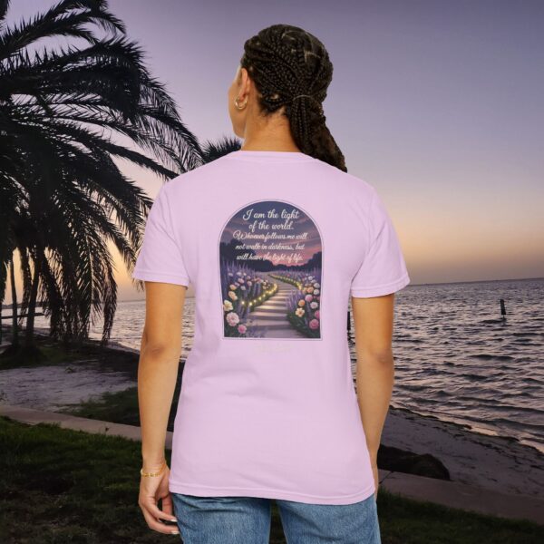 Pink Christian t-shirt with John 8:12 scripture, lit stairway path with flowers and sunset design, worn by a person standing on a sunset beach.