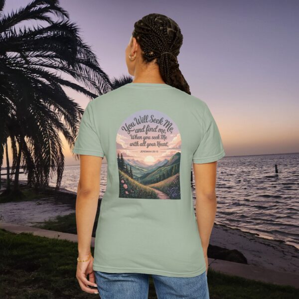 Green Christian t-shirt with Jeremiah 29:13 scripture, mountain valley, and sunset graphic, worn by a person in a serene beach setting.