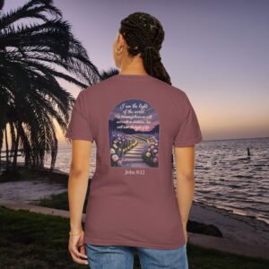 Maroon Christian t-shirt with John 8:12 scripture, lit stairway path with flowers and sunset design, worn by a person standing on a sunset beach.