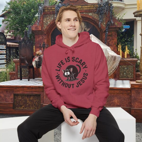 Model on a Halloween set wearing a red Life is Scary Without Jesus Halloween Hoodie, design showing a cute frightened black cat.