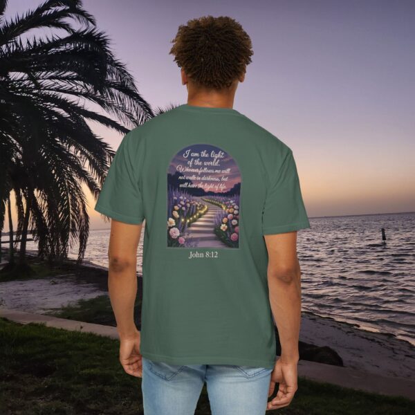Green Christian t-shirt with John 8:12 scripture, lit stairway path with flowers and sunset design, worn by a person standing on a sunset beach.