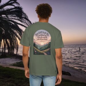 Green Christian t-shirt with Jeremiah 29:13 scripture, mountain valley, and sunset graphic, worn by a person in a serene beach setting.