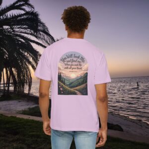 Pink Christian t-shirt with Jeremiah 29:13 scripture, mountain valley, and sunset graphic, worn by a person in a serene beach setting.