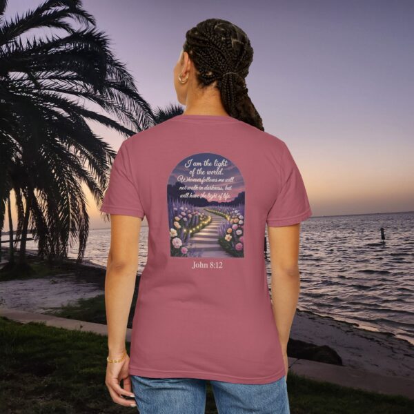 Pink Christian t-shirt with John 8:12 scripture, lit stairway path with flowers and sunset design, worn by a person standing on a sunset beach.