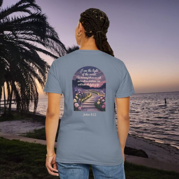 Blue Christian t-shirt with John 8:12 scripture, lit stairway path with flowers and sunset design, worn by a person standing on a sunset beach.