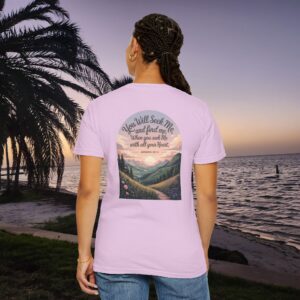 Pink Christian t-shirt with Jeremiah 29:13 scripture, mountain valley, and sunset graphic, worn by a person in a serene beach setting.