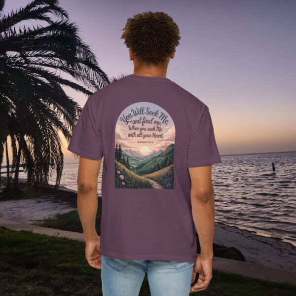 Purple Christian t-shirt with Jeremiah 29:13 scripture, mountain valley, and sunset graphic, worn by a person in a serene beach setting.