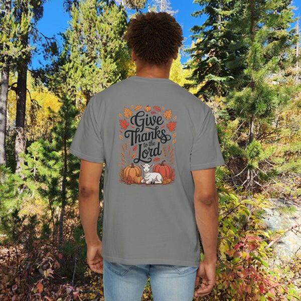 Model in a woods setting wearing a Gray Give Thanks to the Lord t-shirt with Thanksgiving design showing a lamb, pumpkins, and fall leaves.
