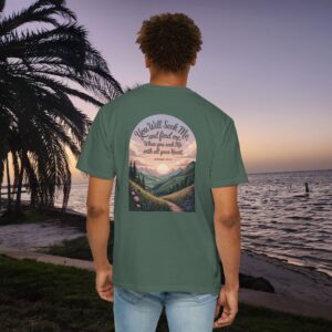 Green Christian t-shirt with Jeremiah 29:13 scripture, mountain valley, and sunset graphic, worn by a person in a serene beach setting.