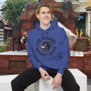Model on a Halloween set wearing a blue Life is Scary Without Jesus Halloween Hoodie, design showing a cute frightened black cat.