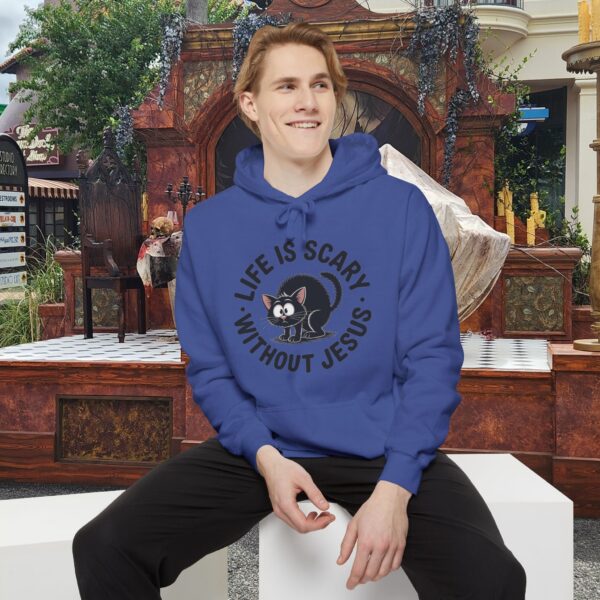 Model on a Halloween set wearing a blue Life is Scary Without Jesus Halloween Hoodie, design showing a cute frightened black cat.