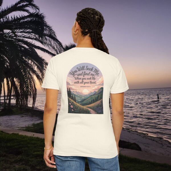 Ivory Christian t-shirt with Jeremiah 29:13 scripture, mountain valley, and sunset graphic, worn by a person in a serene beach setting.