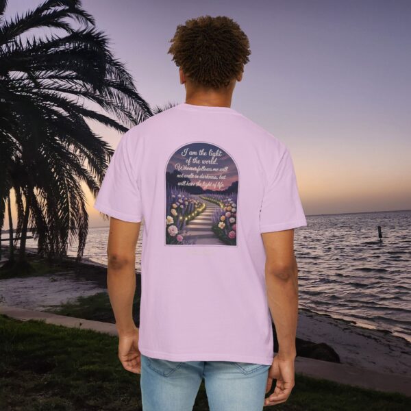 Pink Christian t-shirt with John 8:12 scripture, lit stairway path with flowers and sunset design, worn by a person standing on a sunset beach.