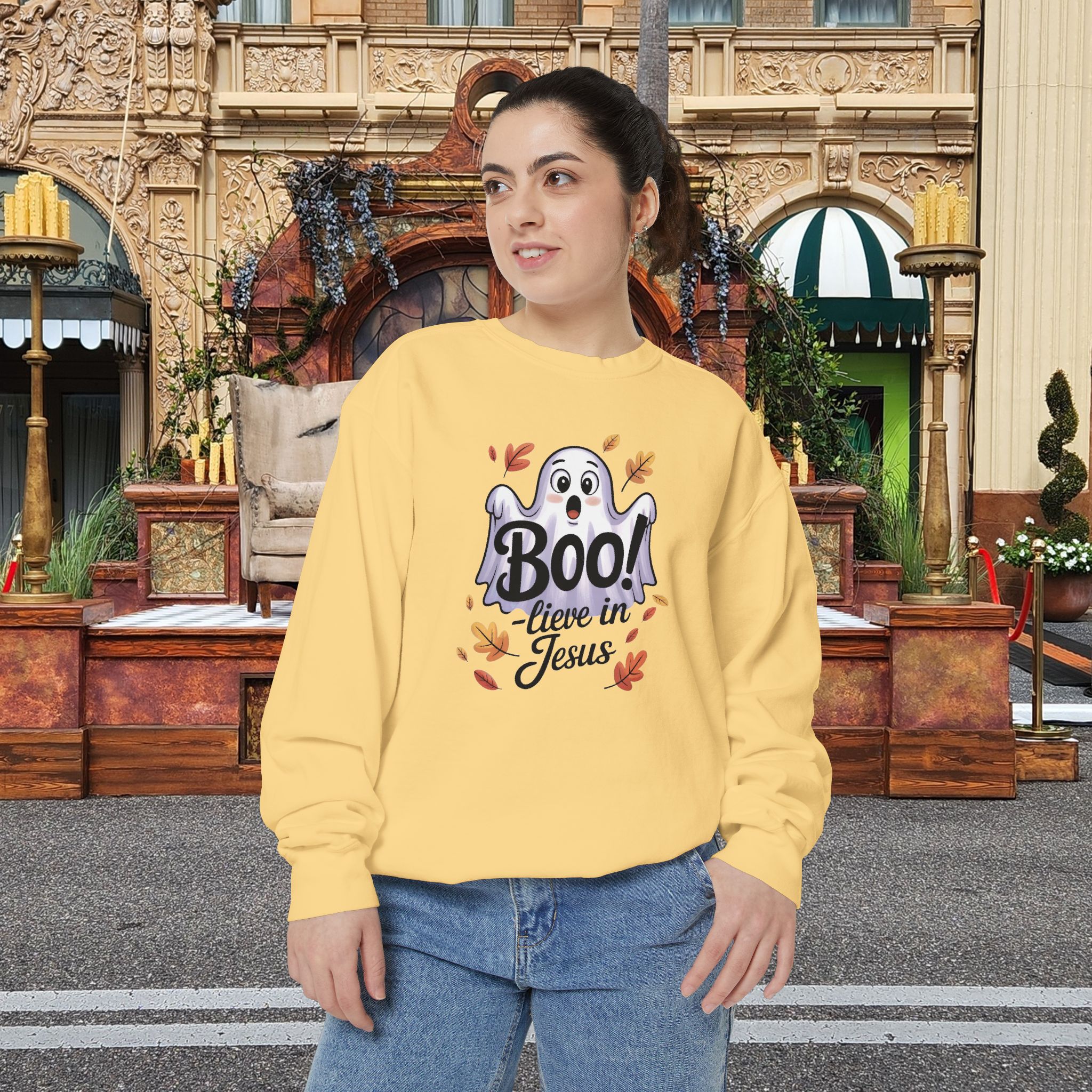 Model on a Halloween set wearing a Yellow Boo! -lieve in Jesus Halloween Sweatshirt, design showing a cute ghost with fall leaves.