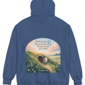 Blue Comfort Colors hoodie sweatshirt with a field and an open tomb with the rock rolled away. Printed on it is 1 Corinthians 15:57 But thanks be to God, who gives us the victory through our Lord Jesus Christ.