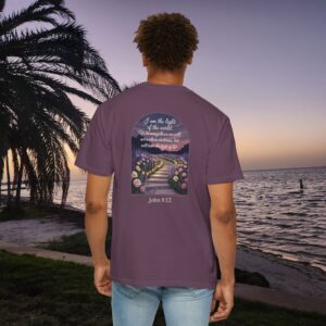 Purple Christian t-shirt with John 8:12 scripture, lit stairway path with flowers and sunset design, worn by a person standing on a sunset beach.