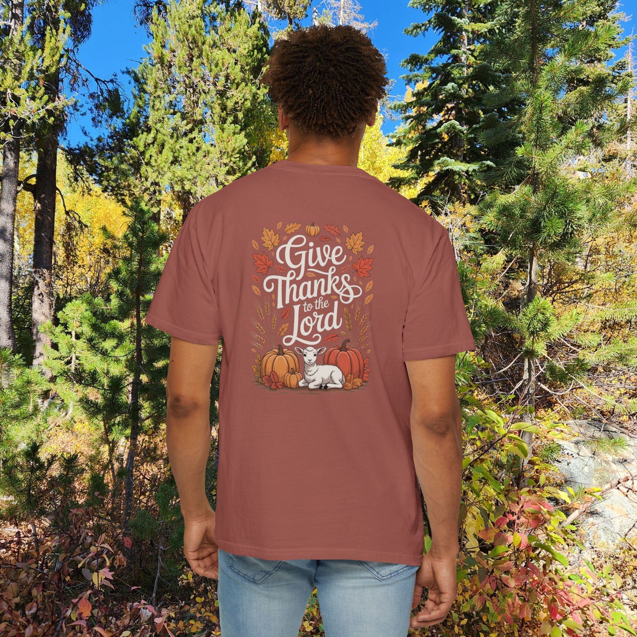 Model in a woods setting wearing a Reed Give Thanks to the Lord t-shirt with Thanksgiving design showing a lamb, pumpkins, and fall leaves.