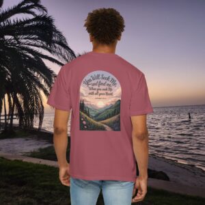 Pink Christian t-shirt with Jeremiah 29:13 scripture, mountain valley, and sunset graphic, worn by a person in a serene beach setting.