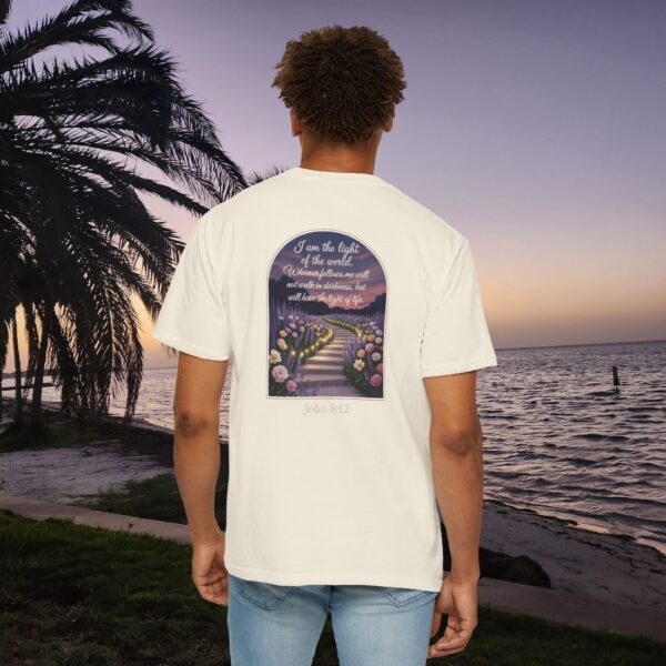 Ivory Christian t-shirt with John 8:12 scripture, lit stairway path with flowers and sunset design, worn by a person standing on a sunset beach.