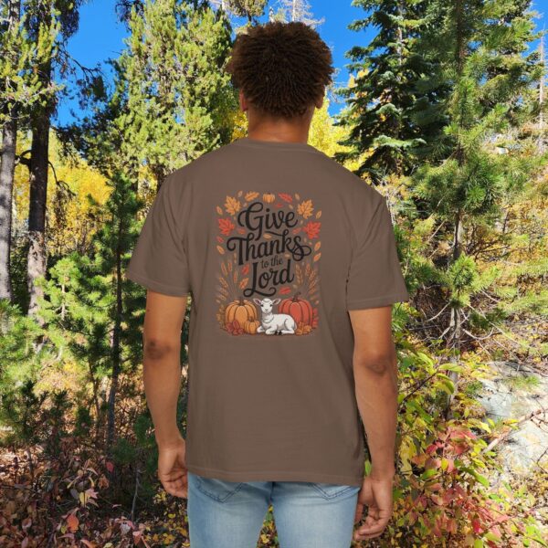 Model in a woods setting wearing a Brown Give Thanks to the Lord t-shirt with Thanksgiving design showing a lamb, pumpkins, and fall leaves.